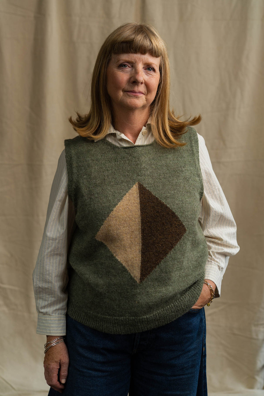 Woman wearing a green sweater vest with a brown diamond pattern against a beige background
