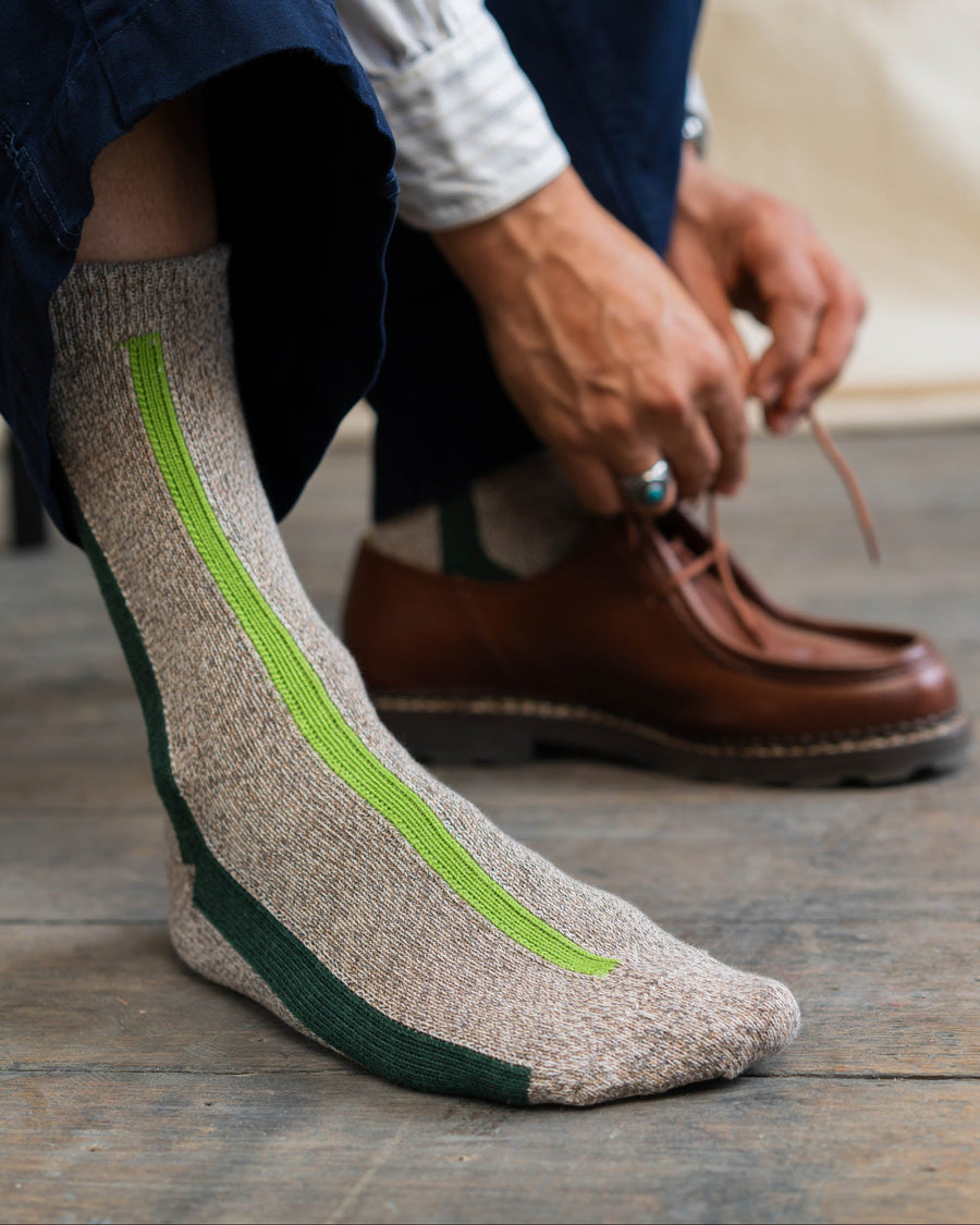 Person wearing a sock with a green vertical stripe, sitting on a wooden floor.