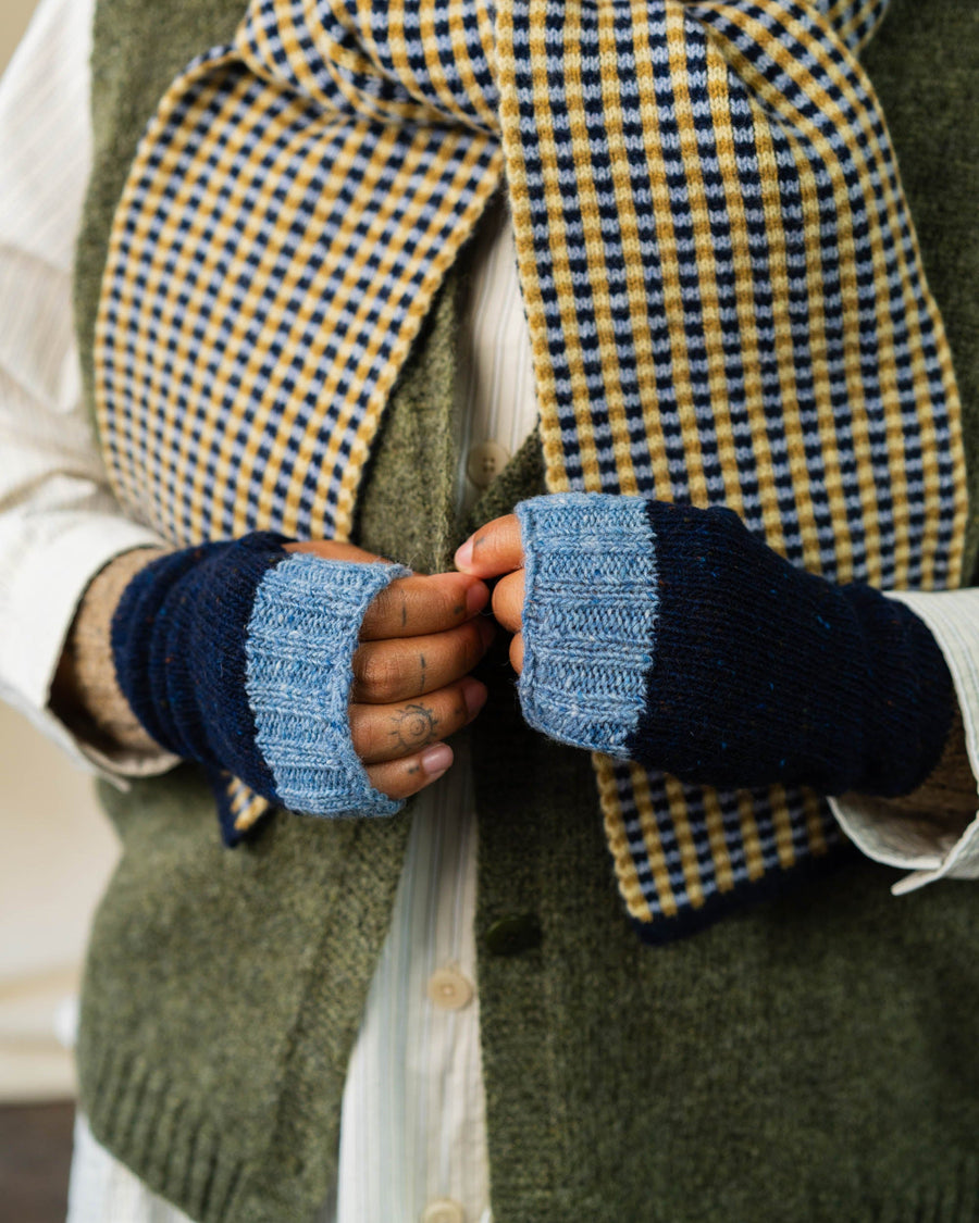 Person wearing a green vest, plaid scarf, and blue fingerless gloves.