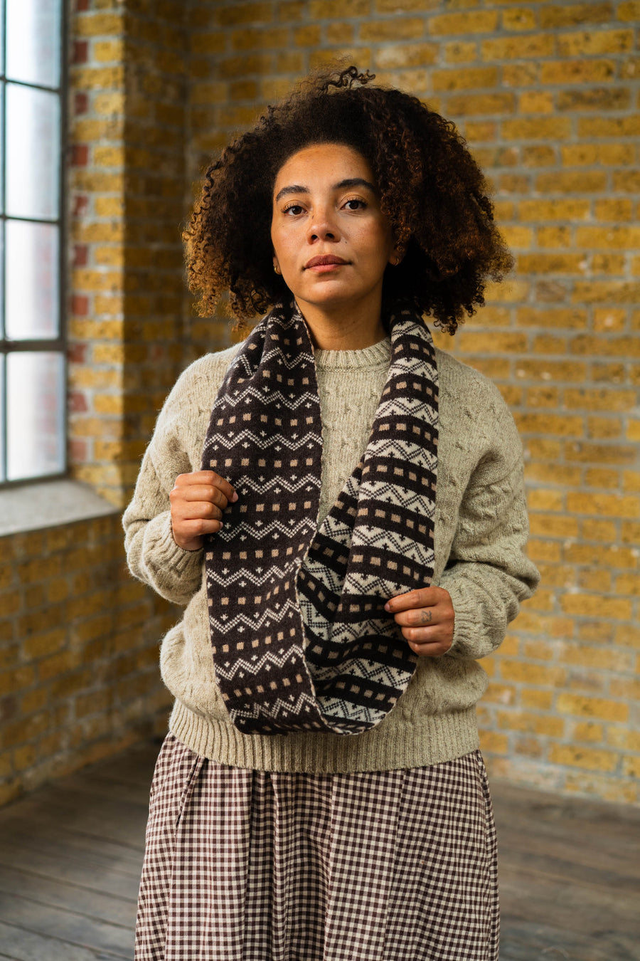 Woman wearing a patterned scarf in front of a brick wall
