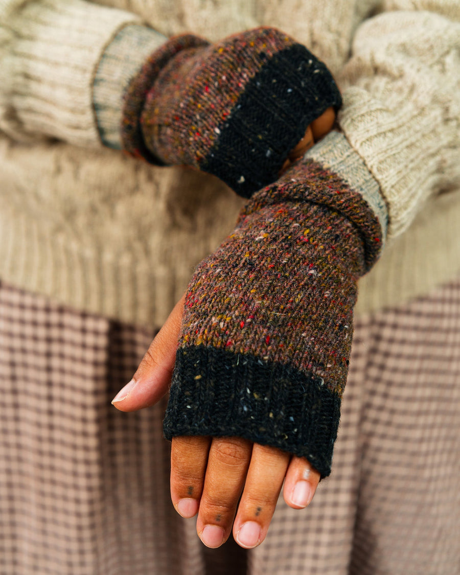 Close-up of a hand wearing a textured brown and black fingerless glove with a plaid fabric background.