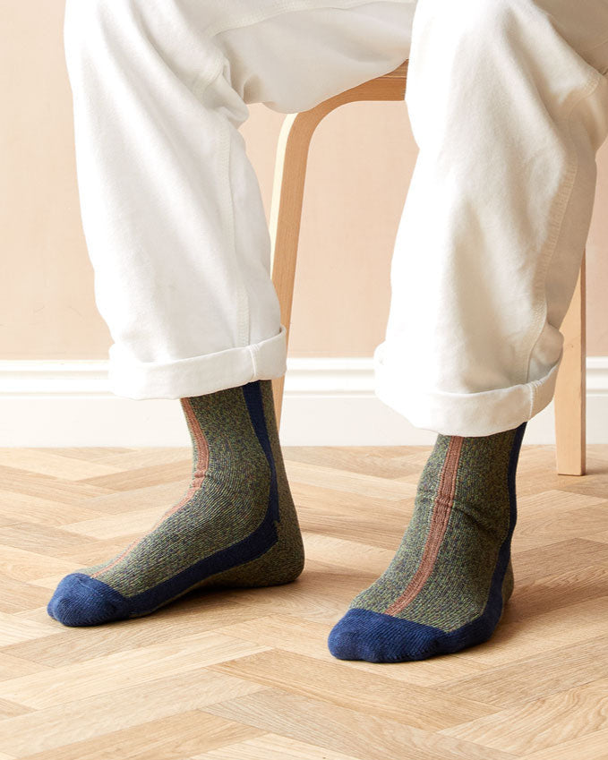 Person wearing patterned socks with blue toes and heels on a wooden floor.